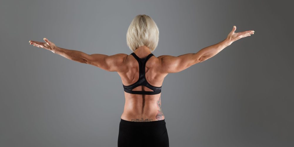 Back view portrait of a muscular adult sportswoman standing with hands outstretched isolated over gray background