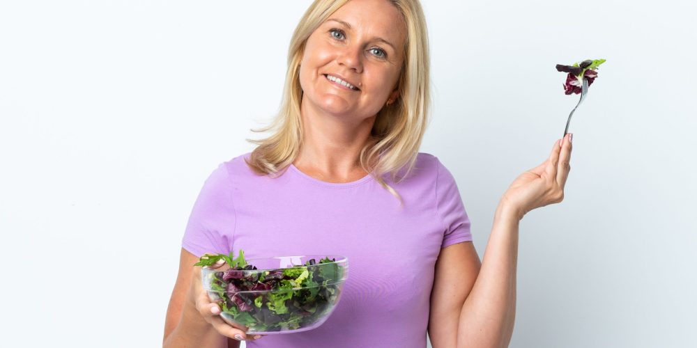 Middle age Lithuanian woman isolated on white background holding a bowl of salad with happy expression